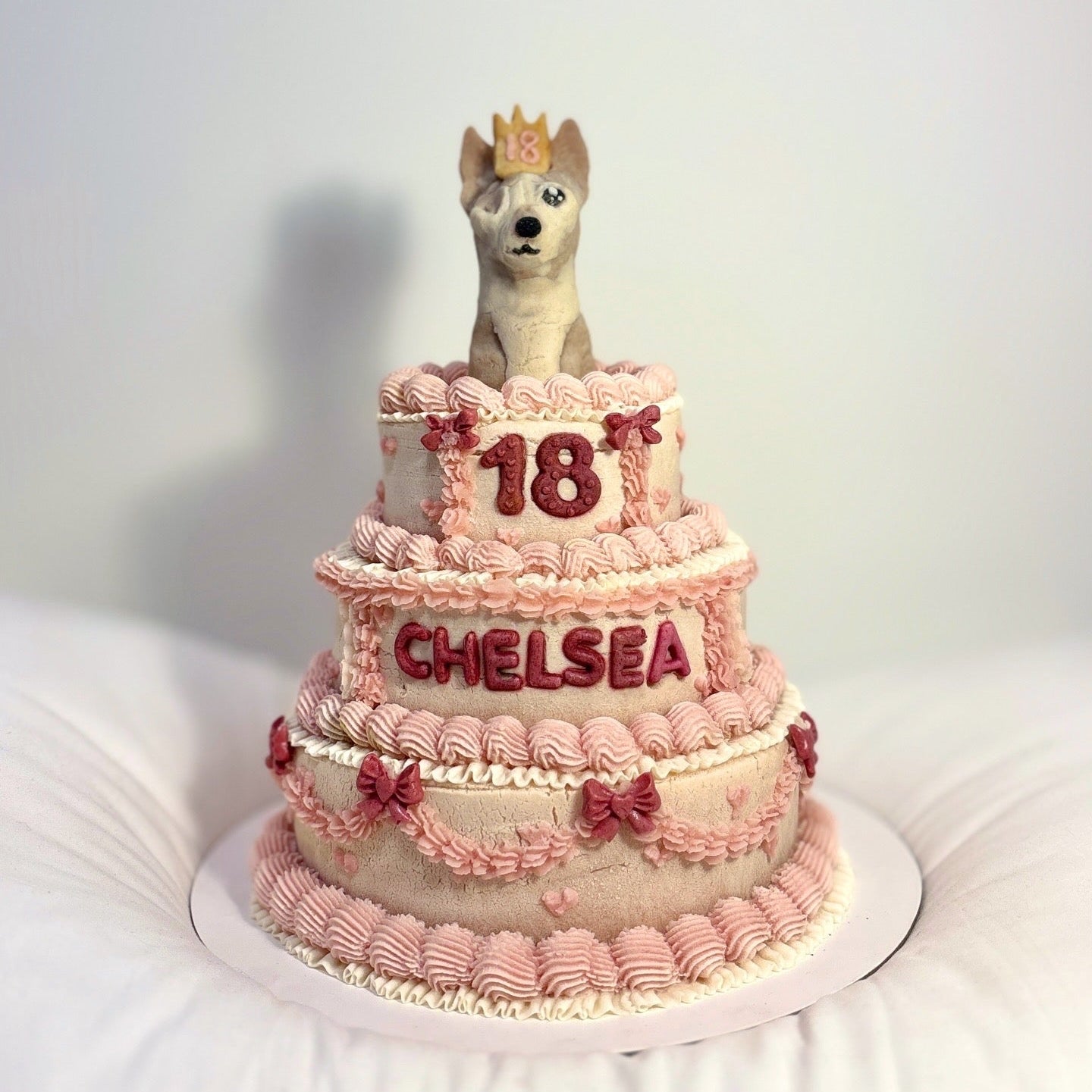 Three-tiered pink birthday cake with a dog figurine and '18 Chelsea' text on a white background
